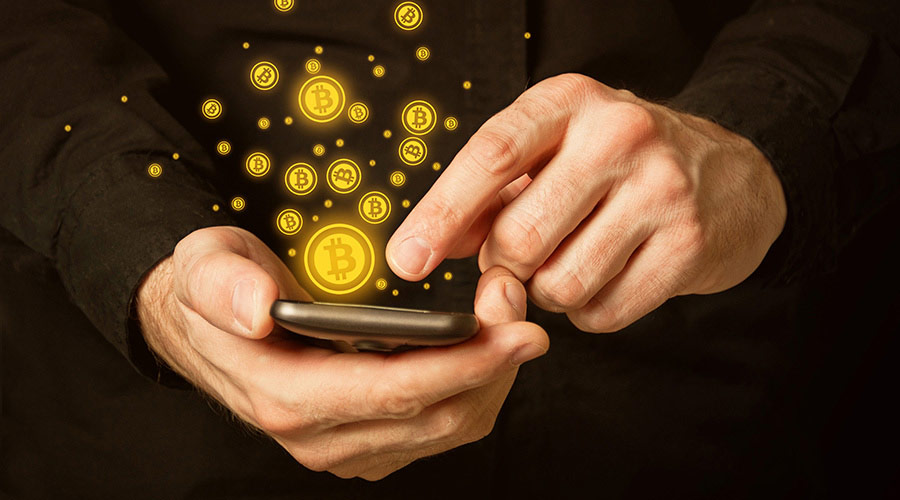 Moedas Digitais: plano detalhe de mãos mexendo em celular, com pequenas moedas vetorizadas saindo da tela, em uma alusão ao formato digital do Bitcoin - que não possui versão física da moeda.