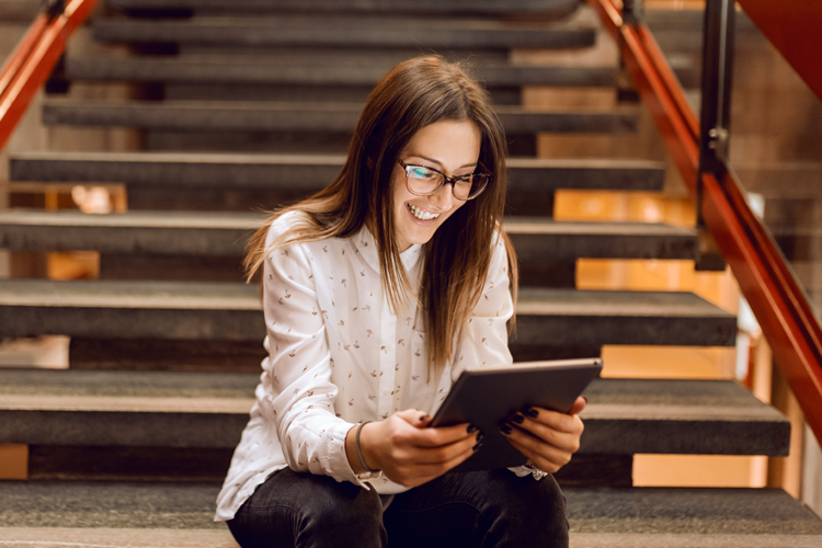 Mulher sentada em escada confere no tablet dicas de apps para estudar